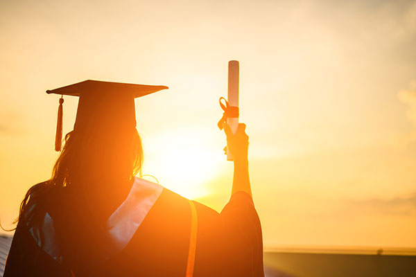 A SAIT graduate holds up her parchment during a sunset.