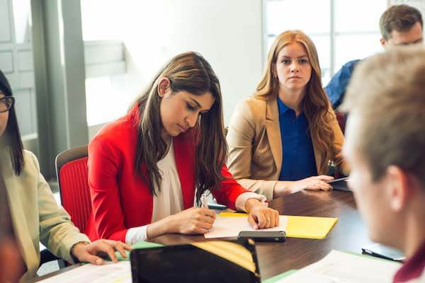 Students sit at a desk studying and taking notes together.