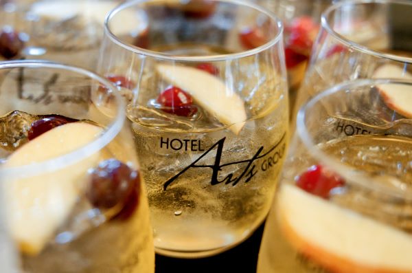 Glasses of a refreshing cocktail featuring apple slices and cherries, with the Hotel Arts logo prominently displayed.