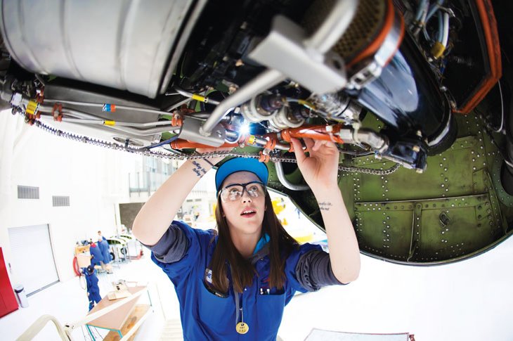 A woman fixing some wires under an aircraft